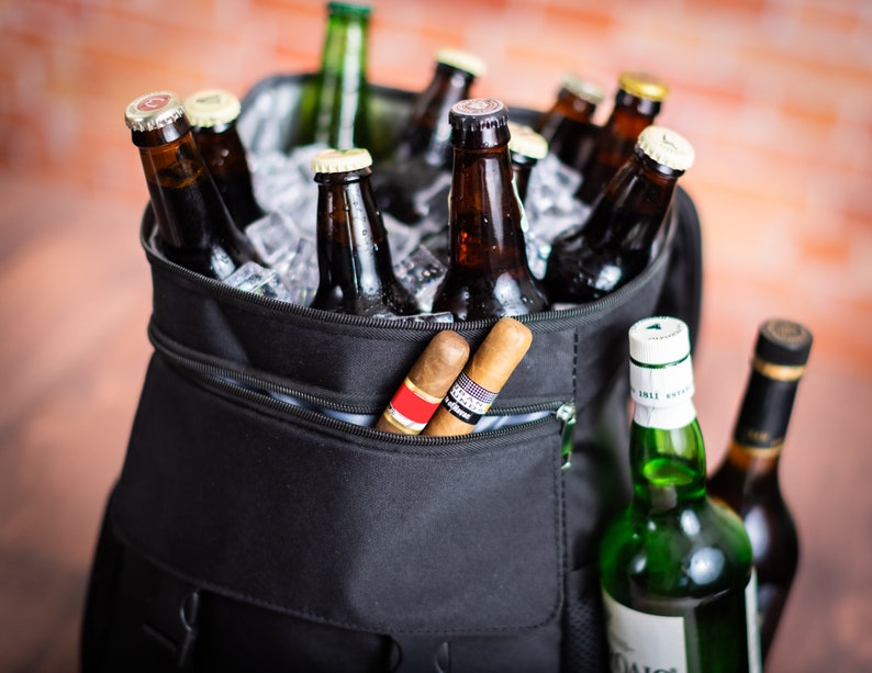 K&ouml;nnte beinhalten: Eine schwarze isolierte K&uuml;hltasche mit einer Rei&szlig;verschlusstasche. Die Tasche ist gef&uuml;llt mit braunen Glasflaschen und Eis. Zwei braune Zigarren ragen aus der Tasche.