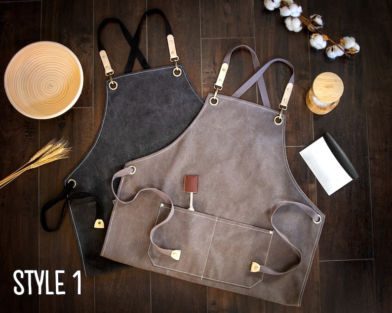 May include: Two canvas aprons with adjustable straps and multiple pockets. The apron on the left is dark gray and the apron on the right is light gray.