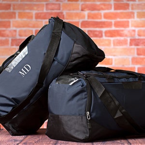 May include: Two navy blue duffel bags with black accents and zippers. The larger bag has the initials "MD" embroidered on the front.