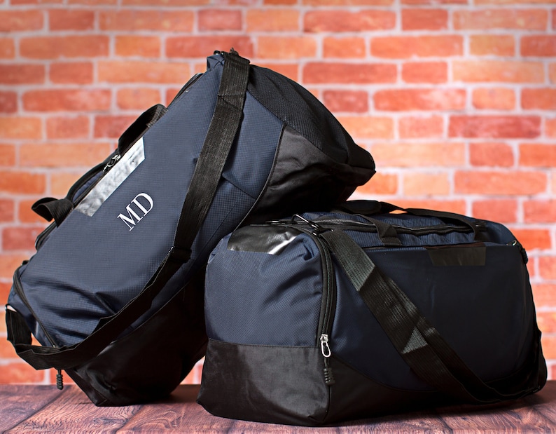May include: Two navy blue duffel bags with black accents and zips. The larger bag has the initials "MD" embroidered on the front.