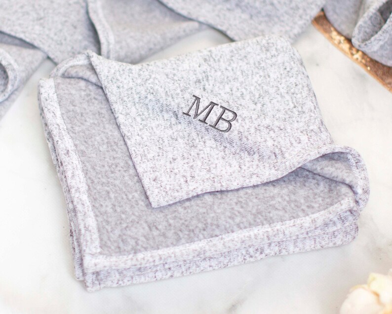 May include: A gray, soft, and cozy blanket with the initials "MB" embroidered in black thread.