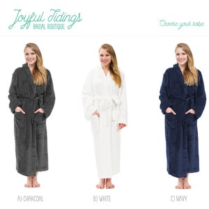 May include: Three women wearing different colored robes. The robes are charcoal, white, and navy blue. The robes are long and have a shawl collar. The women are standing in front of a white background.