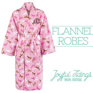May include: Pink flannel robe with a white and brown horse print. The robe has a shawl collar and a tie belt. The robe is monogrammed with the letters "JLC".