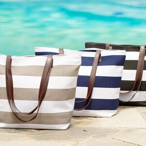 May include: Three striped canvas tote bags with brown leather handles. The bags are in different colors: beige and white, navy blue and white, and black and white.