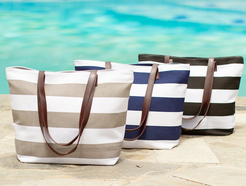 May include: Three striped canvas tote bags with brown leather handles. The bags are in different colors: beige and white, navy blue and white, and black and white.