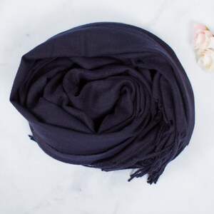 May include: A navy blue scarf with fringe on the ends. The scarf is folded and rolled up.