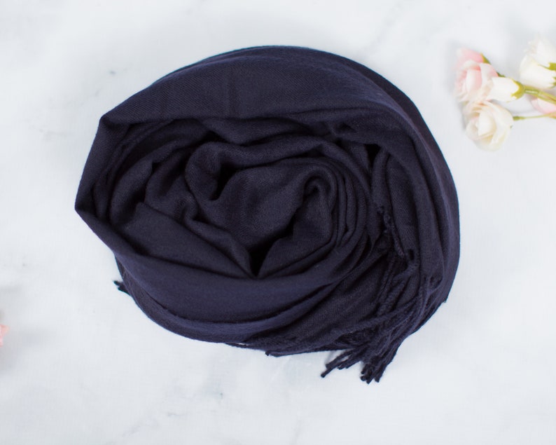 May include: A navy blue scarf with fringe on the ends. The scarf is folded and rolled up.