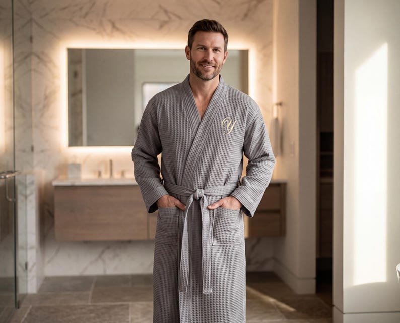 May include: A grey waffle-knit robe featuring a shawl collar, long sleeves, two front patch pockets, and a matching tie belt. The left chest area is embroidered with a white cursive letter Y. The fabric has a distinct grid-like texture.