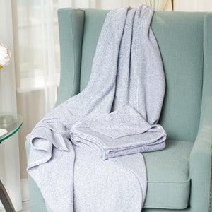 May include: A soft, gray throw blanket draped over a light green armchair. The blanket is folded and has a textured surface.