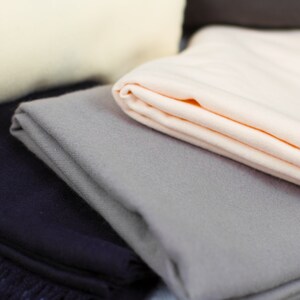 May include: A stack of soft, folded blankets in various colors, including beige, gray, and navy blue. The blankets are made of a soft, plush material and have a subtle texture.