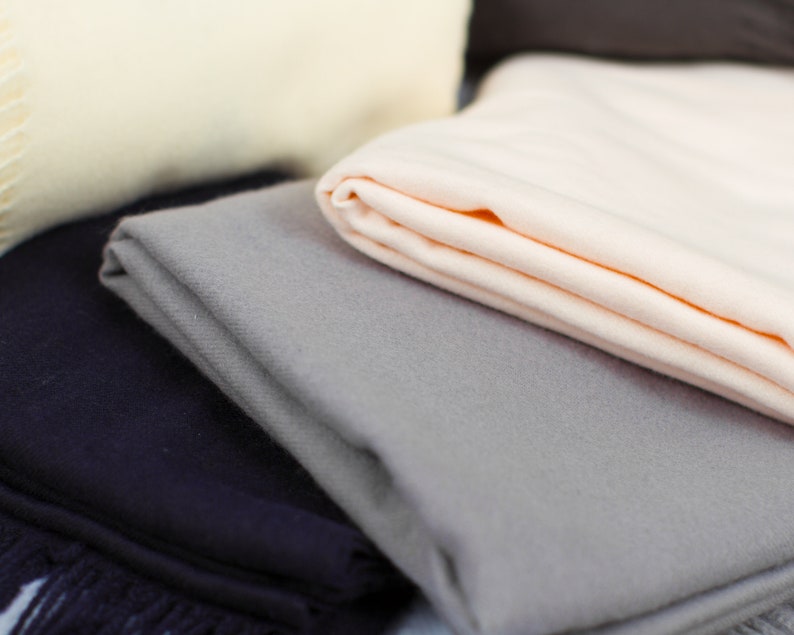 May include: A stack of soft, folded blankets in various colors, including beige, gray, and navy blue. The blankets are made of a soft, plush material and have a subtle texture.