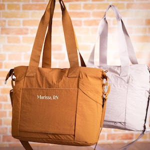 May include: Two tote bags in the image. One is a warm brown color, and the other is a light gray. Both bags have long straps for carrying over the shoulder. The brown bag has the text "Marissa, RN" on the front.