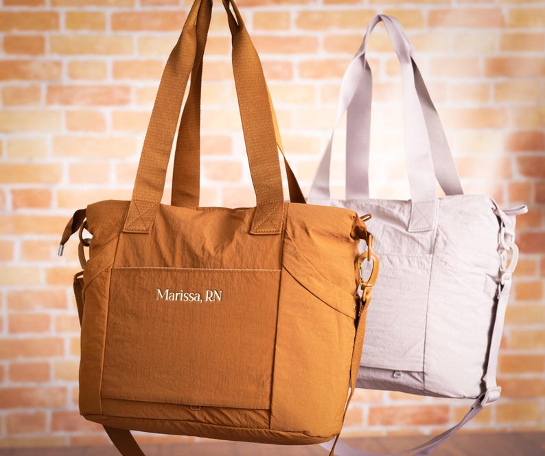 May include: Two tote bags in the image. One is a warm brown color, and the other is a light gray. Both bags have long straps for carrying over the shoulder. The brown bag has the text "Marissa, RN" on the front.