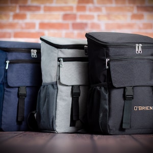 K&ouml;nnte beinhalten: Drei isolierte Rucks&auml;cke in verschiedenen Farben: marineblau, grau und schwarz. Der schwarze Rucksack hat den Text "O'BRIEN" auf der Vorderseite.