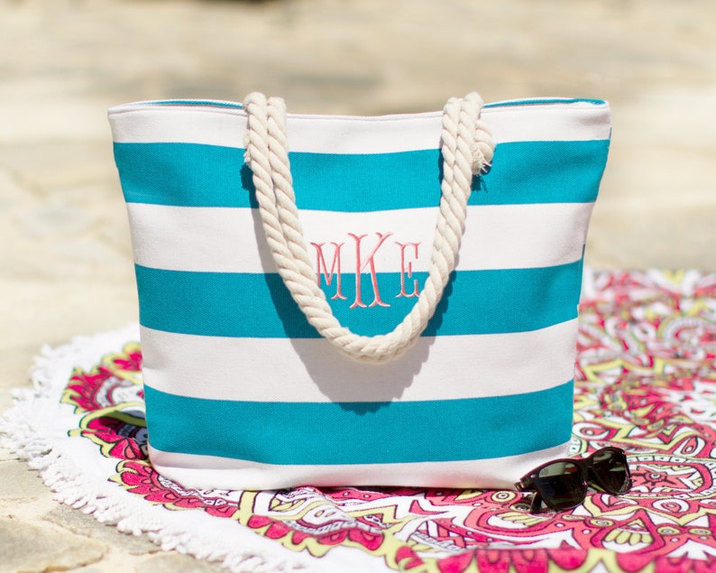 Puede incluir: Una bolsa de lona de rayas blancas y turquesas con asas de cuerda. La bolsa est&aacute; monogramada con las iniciales "MKE" en rosa.