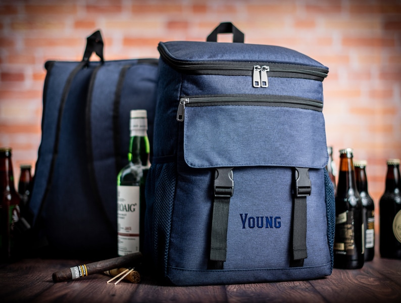 K&ouml;nnte beinhalten: Ein blauer isolierter Rucksack mit einer gro&szlig;en Fronttasche und dem Wort "YOUNG" auf der Vorderseite gestickt. Der Rucksack hat verstellbare Tr&auml;ger und einen Rei&szlig;verschluss.