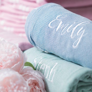 Puede incluir: Dos toallas enrolladas con nombres bordados, Emily y Sarah, en hilo blanco. Las toallas son azul claro y verde claro. Las toallas est&aacute;n rodeadas de peon&iacute;as rosas.