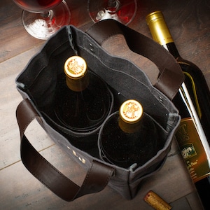 May include: A gray canvas wine tote bag with brown leather handles and two wine bottles inside. The tote bag has two separate compartments for the bottles. The bottles are both red wine and have gold foil caps.