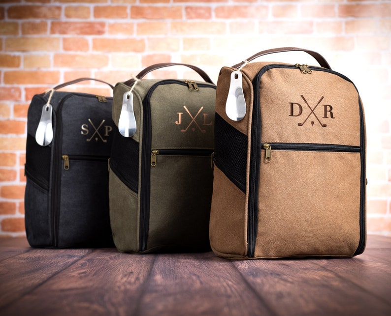 May include: Three personalised golf shoe bags in black, green and brown with embroidered initials and crossed golf clubs. Each bag has a zipped pocket and a shoe horn.