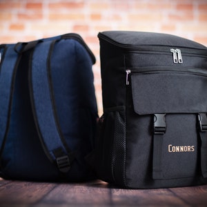 K&ouml;nnte beinhalten: Zwei Rucks&auml;cke, einer blau und einer schwarz. Der schwarze Rucksack hat eine Rei&szlig;verschlusstasche vorne und den Text "Connors" vorne aufgedruckt.