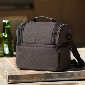 May include: A black insulated lunch bag with a zippered closure and a shoulder strap. The bag is made of a textured fabric and has a rectangular shape.