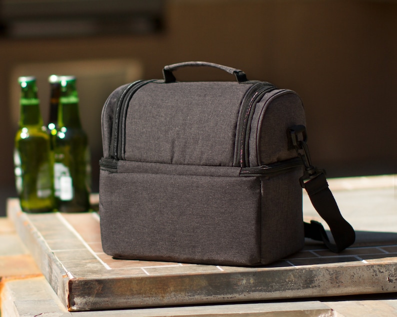 May include: A black insulated lunch bag with a zippered closure and a shoulder strap. The bag is made of a textured fabric and has a rectangular shape.