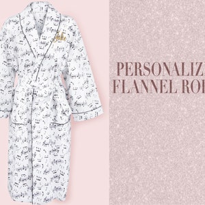 May include: A white flannel robe with a black musical note pattern and black trim. The robe has a personalized name, "Julie", embroidered on the left side of the chest.