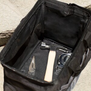 Puede incluir: Una bolsa de herramientas negra con una abertura con cremallera, que contiene un martillo, una cinta m&eacute;trica y un par de alicates.
