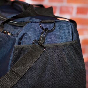 May include: A blue and black duffel bag with a zipped pocket and a black adjustable shoulder strap. The bag has a mesh pocket on the front.