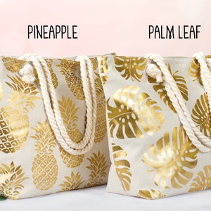 May include: Two canvas tote bags with rope handles. The bag on the left has a gold pineapple pattern on a beige background. The bag on the right has a gold palm leaf pattern on a beige background. The text "Pineapple" is above the left bag and the text "Palm Leaf" is above the right bag.