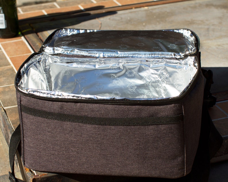 May include: A gray insulated lunch bag with a zippered closure and a black strap. The bag is open and the inside is lined with silver foil.