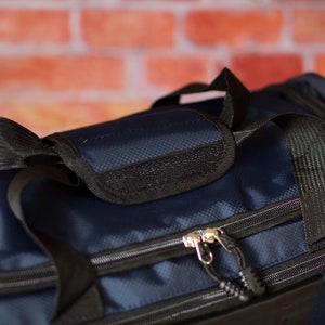 May include: A navy blue duffel bag with black straps and zips. The bag has a small pocket on the top with a black zip.