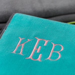 May include: A teal blue microfiber towel with the monogram "KEB" embroidered in pink.