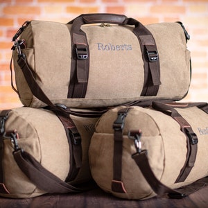 K&ouml;nnte beinhalten: Drei braune Canvas-Reisetaschen mit braunen Ledergriffen und -riemen. Die Taschen sind mit den Namen "Roberts", "Williams" und "Benfield" personalisiert.
