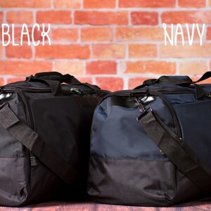 K&ouml;nnte beinhalten: Zwei Reisetaschen, eine schwarz und eine marineblau, mit schwarzen Akzenten. Die Taschen stehen auf einer Holzoberfl&auml;che vor einer Backsteinwand. Die W&ouml;rter "BLACK" und "NAVY" stehen &uuml;ber den Taschen.