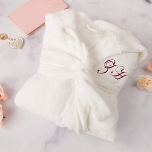 May include: White plush robe with a burgundy embroidered monogram "S.H." on the front.