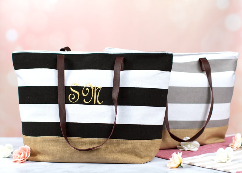 Puede incluir: Dos bolsas de lona a rayas con asas de cuero marr&oacute;n. La bolsa negra y blanca tiene el monograma "SM" bordado en la parte delantera. La bolsa gris y blanca es lisa.