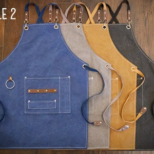 May include: Four canvas aprons in different colors: blue, gray, brown, and black. Each apron has adjustable straps, a large pocket, and a small loop on the side. The aprons are labeled "STYLE 2".