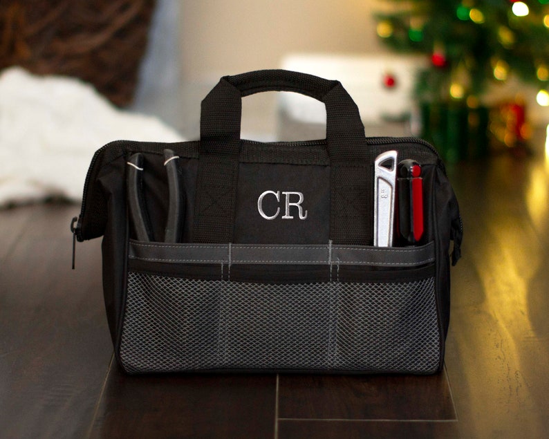 K&ouml;nnte beinhalten: Schwarze Werkzeugtasche mit Rei&szlig;verschluss, einem Netzfach und zwei Seitentaschen. Die Tasche hat einen Griff und die Initialen "CR" sind auf der Vorderseite gestickt.
