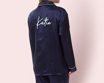 May include: A navy blue satin pajama top with white piping and the name "Katie" embroidered on the back.