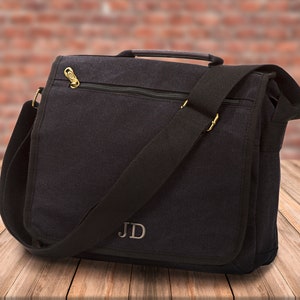 May include: Black canvas messenger bag with a zippered pocket and a long adjustable strap. The bag has a monogrammed "JD" on the front.