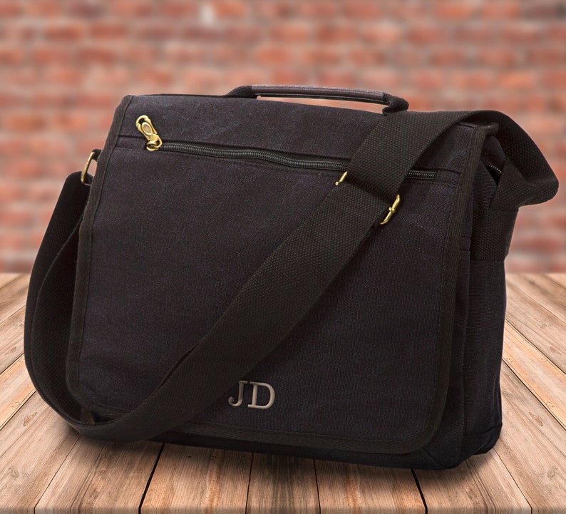 May include: Black canvas messenger bag with a zippered pocket and a long adjustable strap. The bag has a monogrammed "JD" on the front.