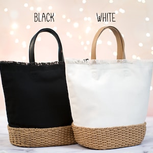 May include: Two tote bags with frayed edges and a woven bottom. The bag on the left is black with a black leather handle. The bag on the right is white with a tan leather handle. The text "BLACK" is above the black bag and the text "WHITE" is above the white bag.