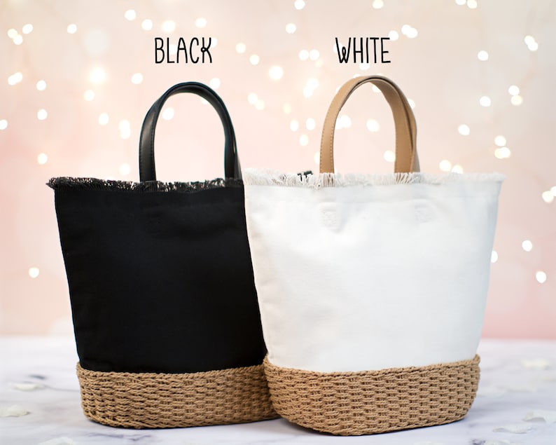 May include: Two tote bags with frayed edges and a woven bottom. The bag on the left is black with a black leather handle. The bag on the right is white with a tan leather handle. The text "BLACK" is above the black bag and the text "WHITE" is above the white bag.