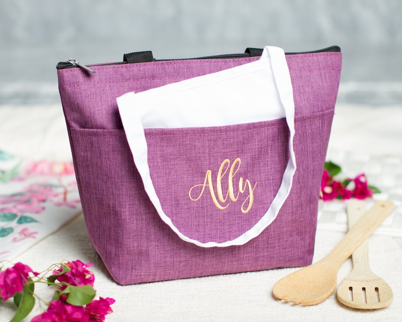 May include: Purple insulated lunch bag with a white zipper pull and a white handle. The bag has the name "Ally" embroidered on the front in gold thread.