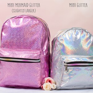 May include: Two iridescent glitter backpacks. The larger backpack is pink and says "Mini Mermaid Glitter (Slightly Larger)". The smaller backpack is silver and says "Mini Glitter".