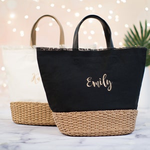 May include: Two personalized tote bags with woven straw bottoms. The bag on the left is white with the name "Kara" embroidered in gold. The bag on the right is black with the name "Emily" embroidered in gold.