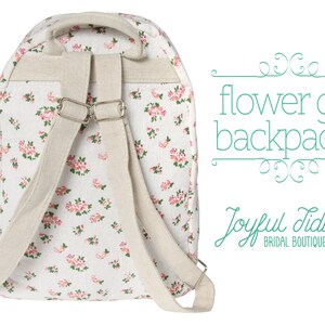 May include: A white canvas backpack with a floral pattern. The backpack has adjustable straps and a zipper closure. The text "flower girl backpacks" and "Joyful Tidings BRIDAL BOUTIQUE" is visible in the image.