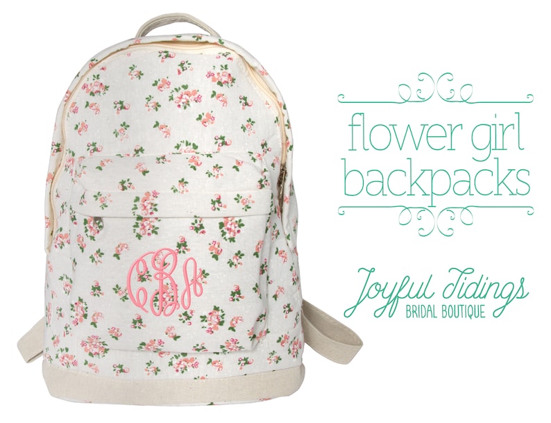 May include: A white canvas backpack with a pink floral pattern and a pink monogram. The backpack has a zipper closure and adjustable straps. The text "flower girl backpacks" and "Joyful Tidings BRIDAL BOUTIQUE" is visible in the image.