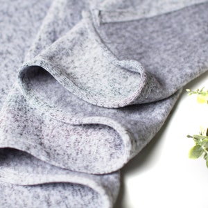 May include: Close-up of a gray, textured fabric with a soft, crinkled appearance. The fabric is folded over itself, creating a series of folds and creases.